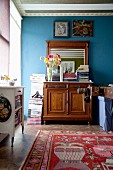 Stacked magazines on top of antique cabinet with mirror against blue wall
