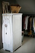 Kleiderbügel mit weißem Kleid an weiss lackierten Schrank aufgehängt, oberhalb Korb, im Hintergrund Kleiderständer