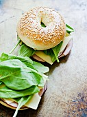 A sesame seed bagel topped with ham, Asiago cheese and lambs lettuce