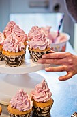A hand placing cupcakes decorated with buttercream on a cake stand