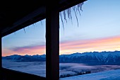 Blick aus vereister Hütte auf verschneite Berggipfel und auf das Nebelmeer