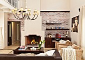 Interior in elegant, country-house style with fireplace, painted faux brickwork, chandelier with lampshades above lounge area and partially visible gallery