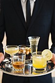 Junger Kellner serviert verschiedene Drinks auf einem Silbertablett
