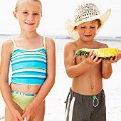 A boy and a girl on a beach with a slice of pineapple