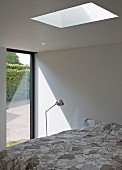 Modernes Schlafzimmer - Bett unter Oberlicht in Decke, seitlich Stehleuchte vor Terrassentür