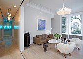 Blick vom Gang in offenes Wohnzimmer mit extravaganten Sesseln und weißem Couchtisch vor braunem Ledersofa