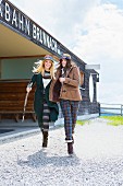Two women wearing winter clothes walking in front of a cable car station