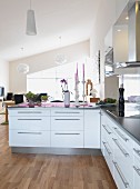 Fitted kitchen with white cabinets and stainless steel strip handles in open-plan interior
