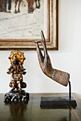 Sculpture of hand and figurine on antique cabinet in front of corner of painting