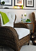 Wicker armchair with white cushions and side table with wine bottle and wine glasses in candlelight atmosphere
