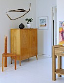 Half-height, fifties-style cabinet in pale, solid wood and hand-crafted chair in simple room