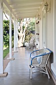 White rattan chair against wall of cottage veranda with white wooden structure