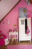 White wardrobe and console table with curved legs against pink-painted gable wall in vintage-style girl's bedroom