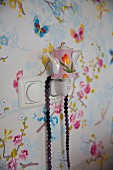 Night light shaped like vintage teapot against wallpaper with pattern of butterflies