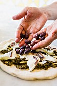 Olives being placed on a kale pizza