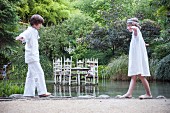Zwei Kinder balancieren am Teich entlang, im Hintergrund Tisch im Gewässer stehend