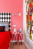 Eclectic bedroom with red, patterned wallpaper, black and white bed headboard, whimsical bedside table and modern artwork