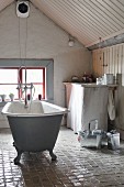 Freistehende Vintage Badewanne auf glasiertem Keramik-Fliesenboden im Bad unter dem Dach, Fenster in Giebelwand