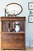 Old bureau with bouquet in white jug on fold-down desk in rustic interior