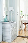 White table lamp on chest of drawers with pale varnish in corner of room next to open doorway