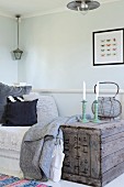 White candles in candlesticks on vintage wooden crate next to daybed in corner of simple room