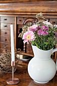 Bouquet of summer flowers in white china jug and candle in copper candlestick