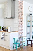 Retro child's chair and step stool painted turquoise between modern kitchen counter with stainless steel extractor hood and glass display cabinet