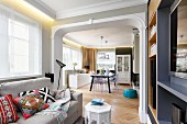 Pale couch with Moroccan scatter cushions in lounge area and view through open doorway into dining room in open-plan interior with art nouveau elements