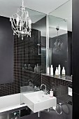 Small chandelier in designer bathroom with black mosaic tiles