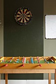Dartboard on dark green wall behind table football set
