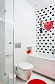 Toilette neben der Badewanne in weißem Badezimmer mit gepunkteter Wand