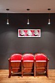 Red, retro cinema seats below Andy Warhol pop art picture on dark grey wall and designer pendant lamps