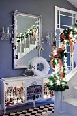 Staircase balustrade decorated with fir branches in front of mirror on grey wall above sideboard