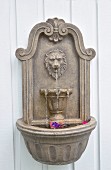 Stone pool with water spout on white, wooden wall