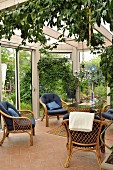 Wicker chairs with blue cushions on pale terracotta floor tiles in conservatory with view of garden