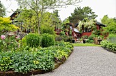 Gravel path lined by lush herbaceous borders leading to house and summer house