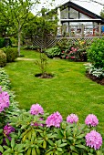 Rasenfläche in gepflegtem Garten vor modernem Holzhaus mit verglaster Giebelfassade; Rhododendron im Vordergrund