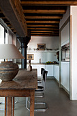 Tischleuchte auf rustikalem Holztisch und Klassiker Freischwinger in offener moderner Küche mit traditioneller Metallstütze