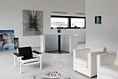 weiße Designersessel und schwarzer Stuhl in minimalistischem Loungebereich, im Hintergrund Treppenabgang mit kreisförmiger Brüstungswand