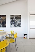 Gelbe Retro Stühle um Tisch, im Hintergrund Bilder an Wand, in modernem Ambiente mit Fliesenboden