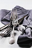 Old silver cutlery with a grey napkin on a white table cloth