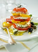 A stack of sliced tomatoes, peppers and mozzarella with olives and capers