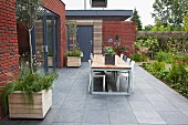 Tisch und Stühle auf Terrasse mit grauem Fliesenboden, vor modernem Anbau aus Ziegel