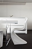 White Panton chairs at table with chrome frame in front of free-standing, designer kitchen counter