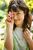 Young woman holding pink flower in front of eye