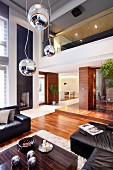 Pendelleuchten mit Kugelschirm in verschiedener Höhe über Bodentisch aus Makassar Holz und schwarze Ledersofagarnitur in elegantem Wohnraum mit Galerie