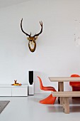 Dining table and orange classic chairs below hunting trophy on wall