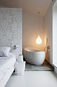 Bed and side table in front of partition; free-standing bathtub in corner below pendant lamp