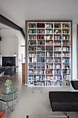 Hohes Bücherregal mit Leiter vor Raumteiler, im Vordergrund Retro Beistelltisch in Loft Wohnraum
