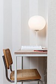 White, spherical table lamp on delicate table and cantilever, cane chair